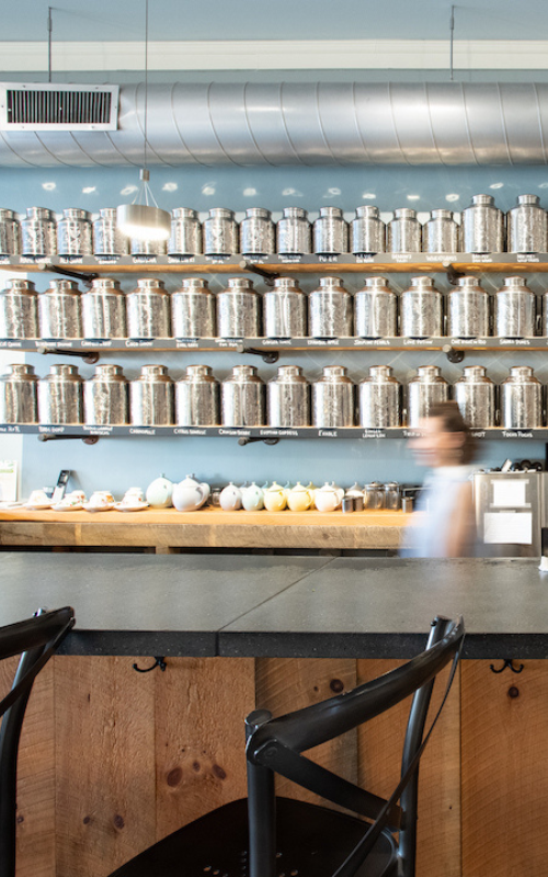 tea bar at saratoga tea and honey co showing wall of silver tea tins and blurred motion of a tea tender
