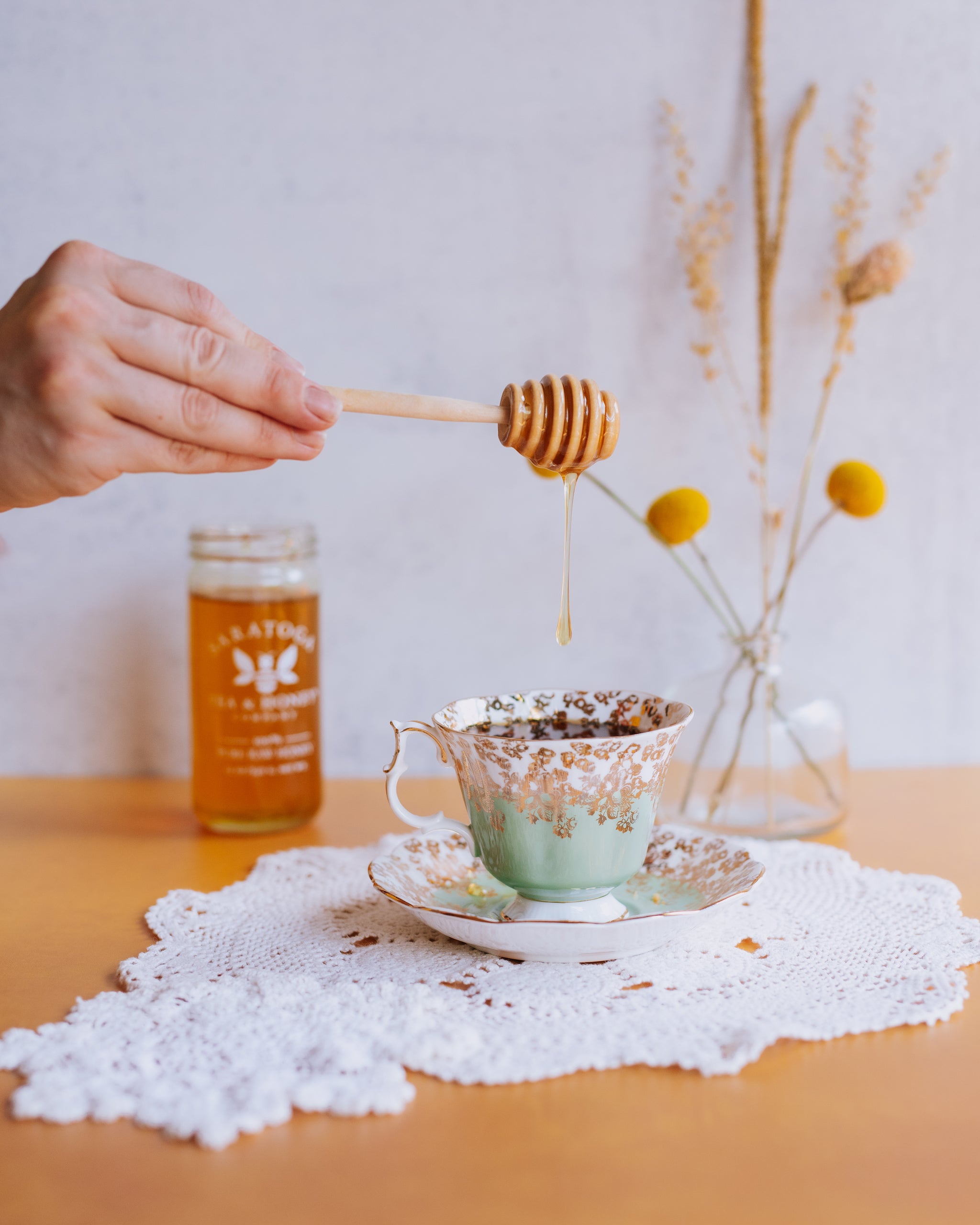 hand drizzling honey into vintage teacup using a wooden honey dipper