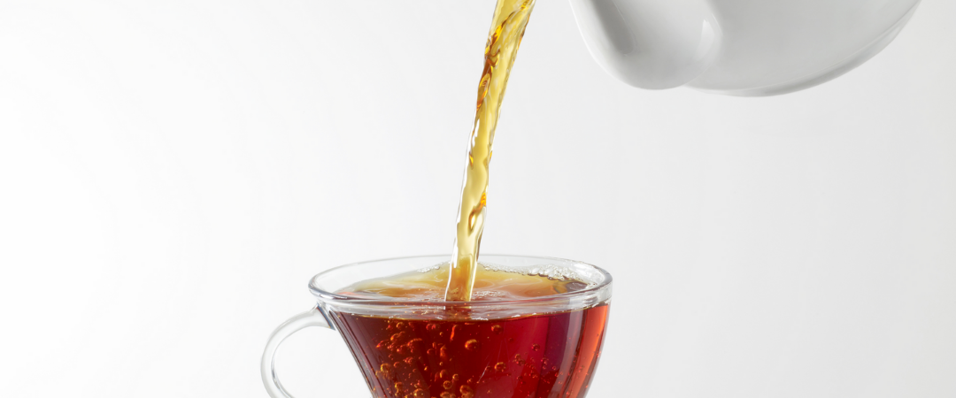 tea being poured from a white teapot into a glass cup