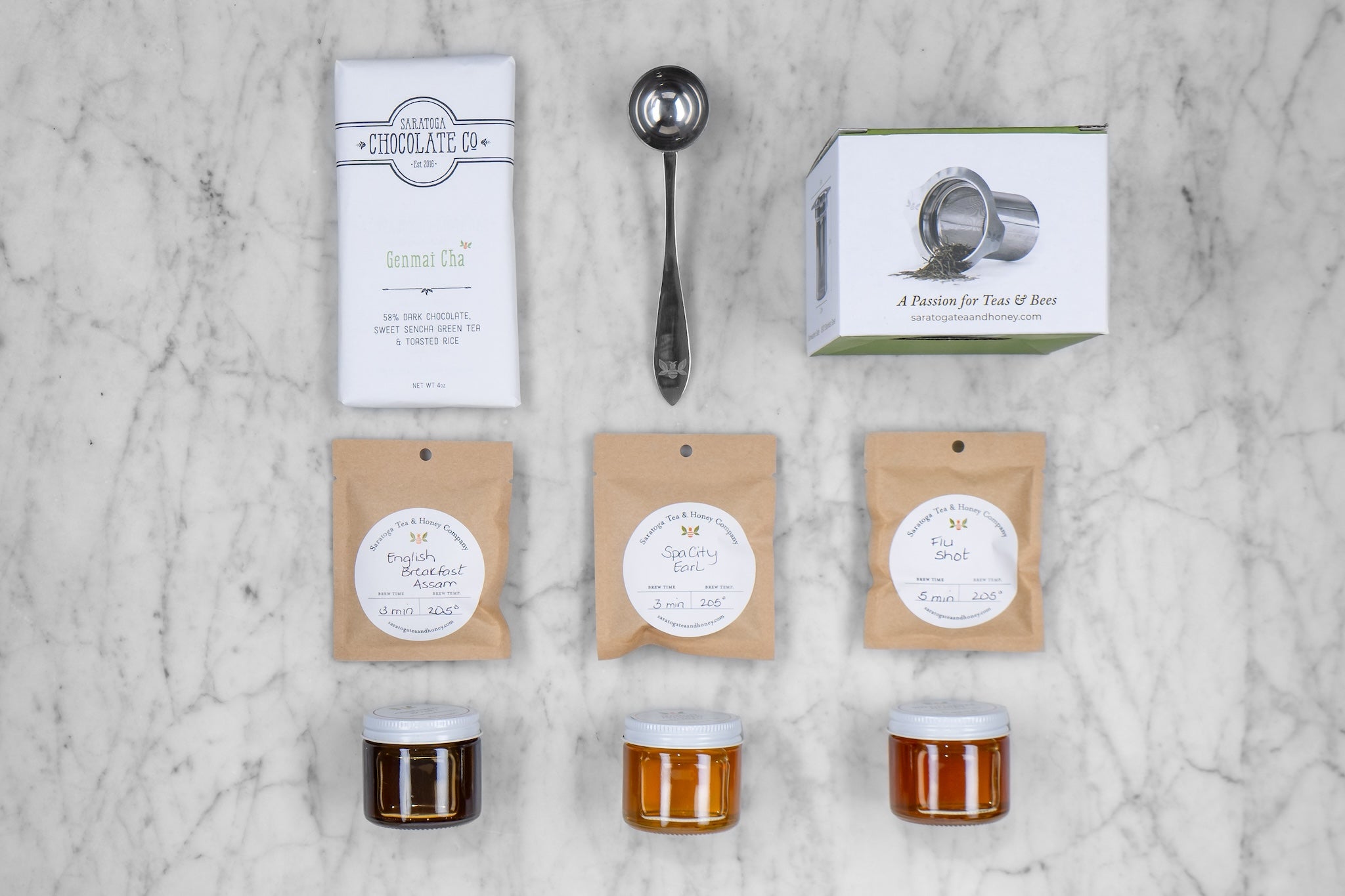 flat lay of included items in a Honey Bee Gift Set: three sample teas, three sample honeys, a stainless steel infuser, tea scoop, and local chocolate bar