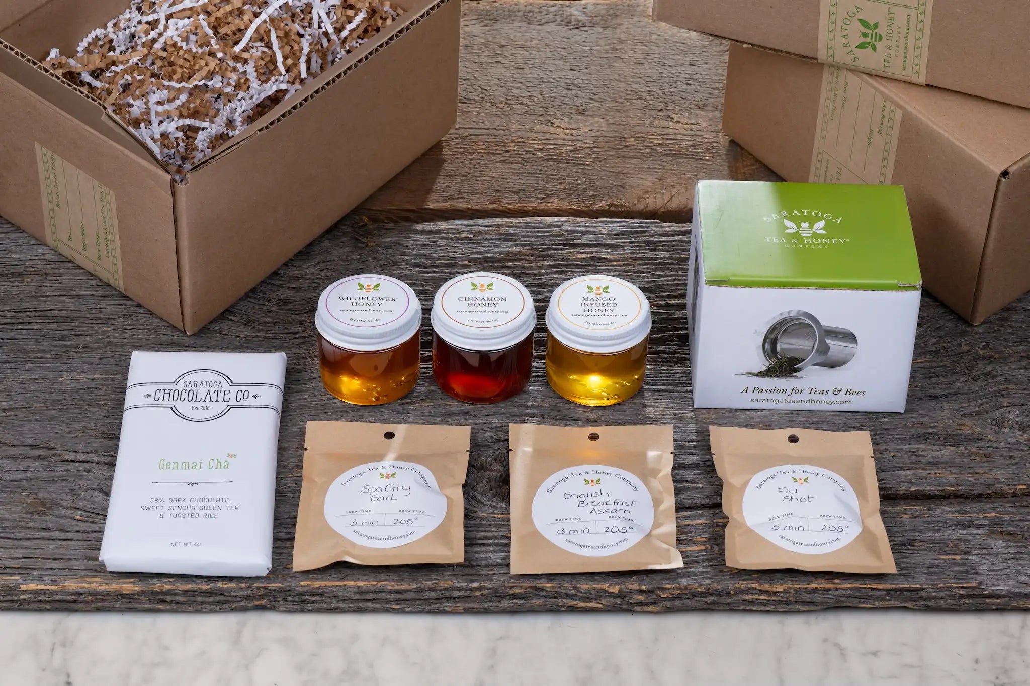 Honey Bee subscription box with three small honeys, three small tea samples, and local treat on a wood and marble background
