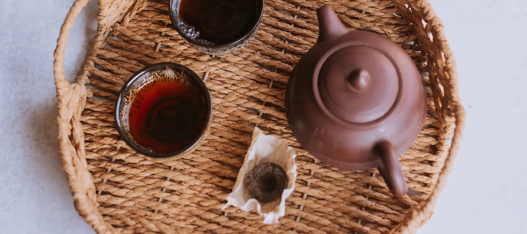yixing pot with brewed small cups of aged tea and a tuocha (nest) of shou pu erh
