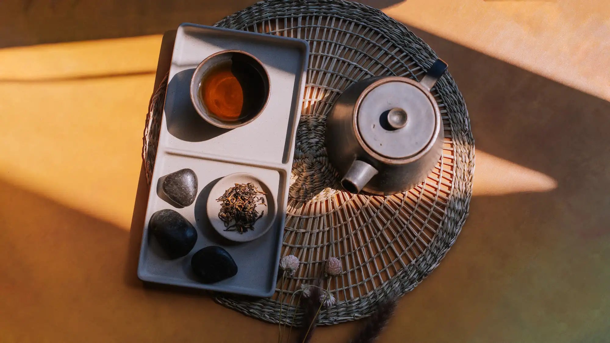 aerial shot of brewed black tea in a handleless cup next to loose leaf black tea with a modern ceramic grey teapot