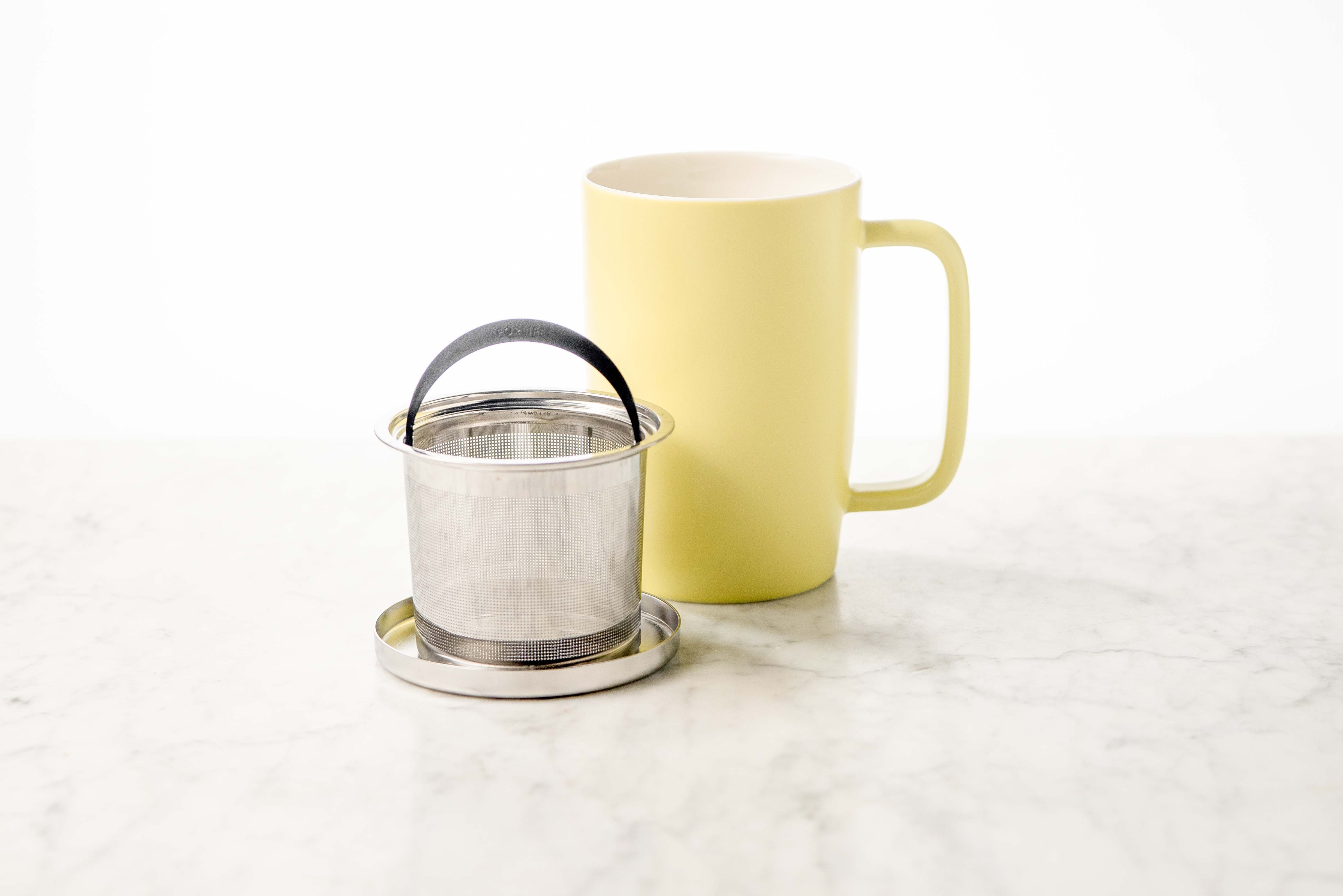 showing three parts of the dew brew in mug: stainless steel lid and basket rest, stainless steel infuser basket, and yellow ceramic mug with large handle