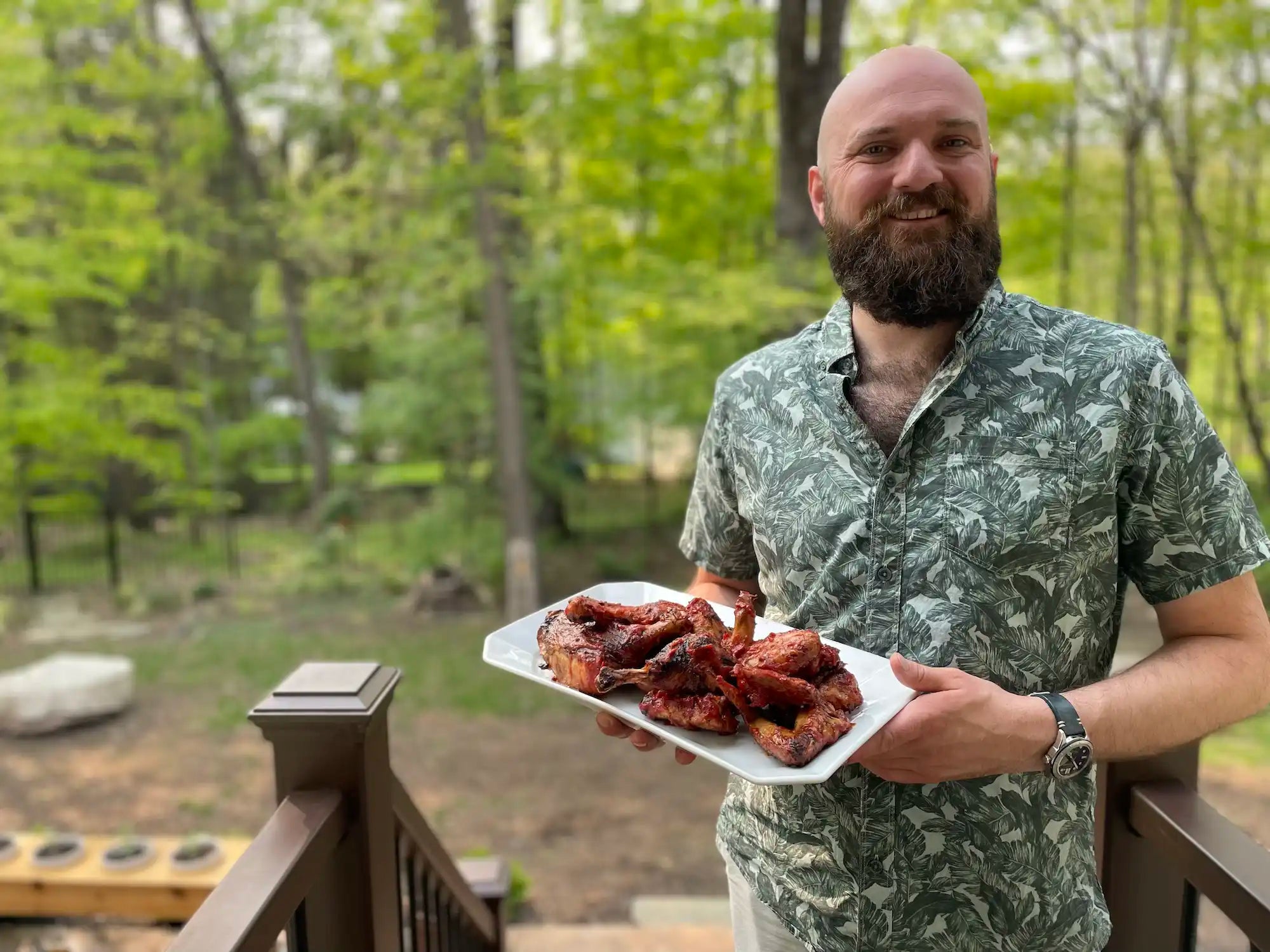 man in leaf print shirt holding platter of honey bbq grilled chicken
