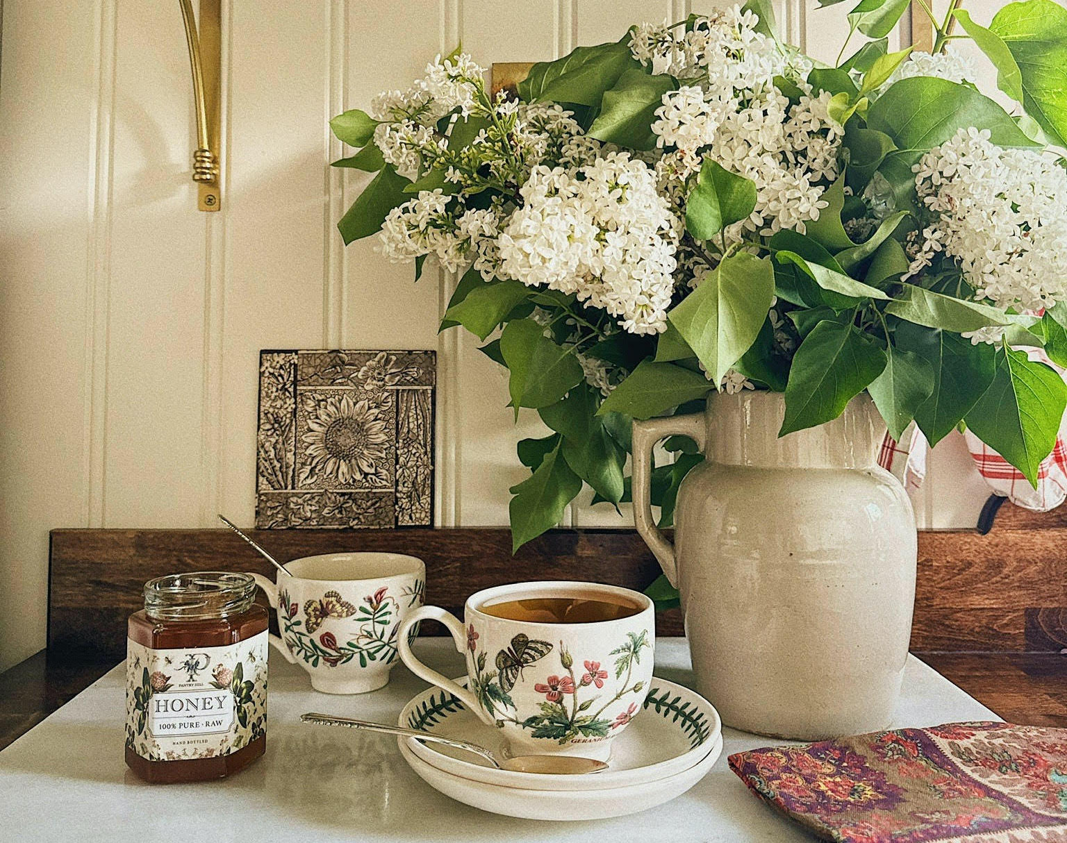 aesthetic vignette of a cup of the Pantry Hill Blend black tea next to a rustic vase of hydrangeas and a jar of honey