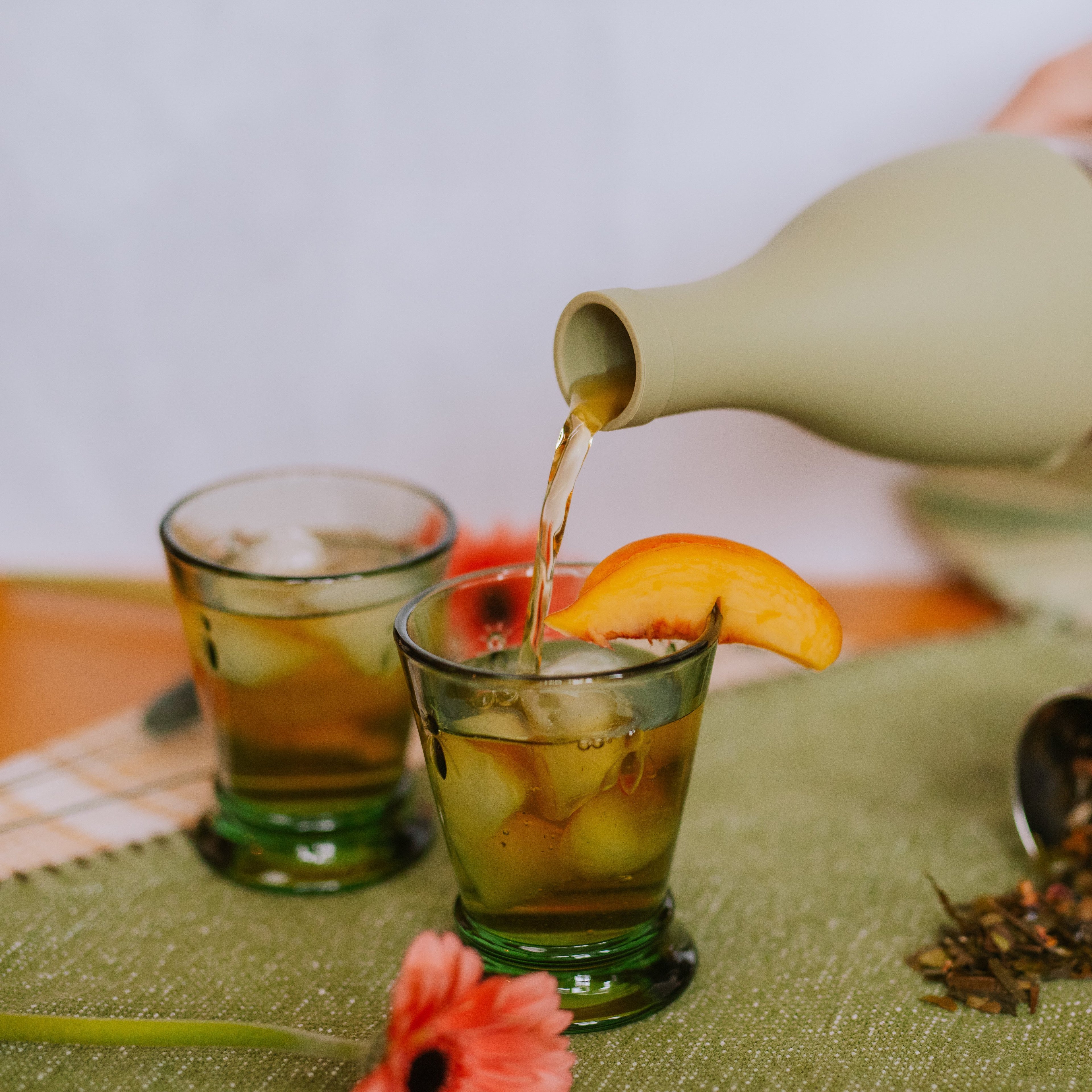 Iced tea pouring from a pitcher into a cup garnished with a peach slice.