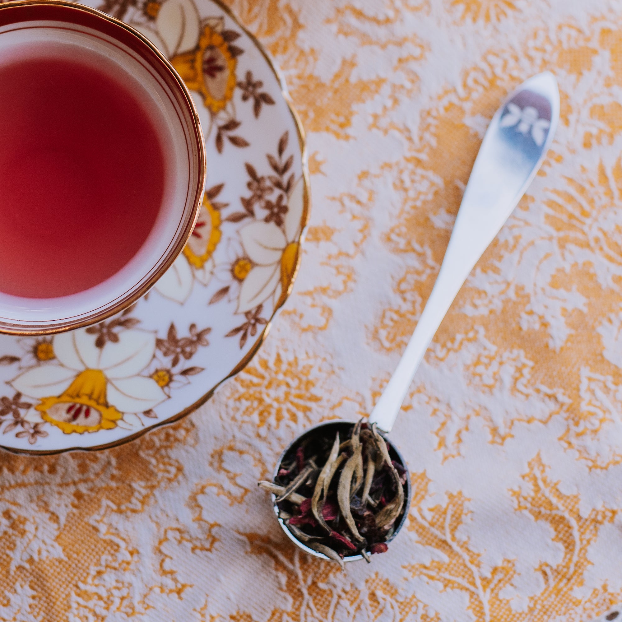 tea scoop of white tea with hibiscus next to vintage tea cup with tea