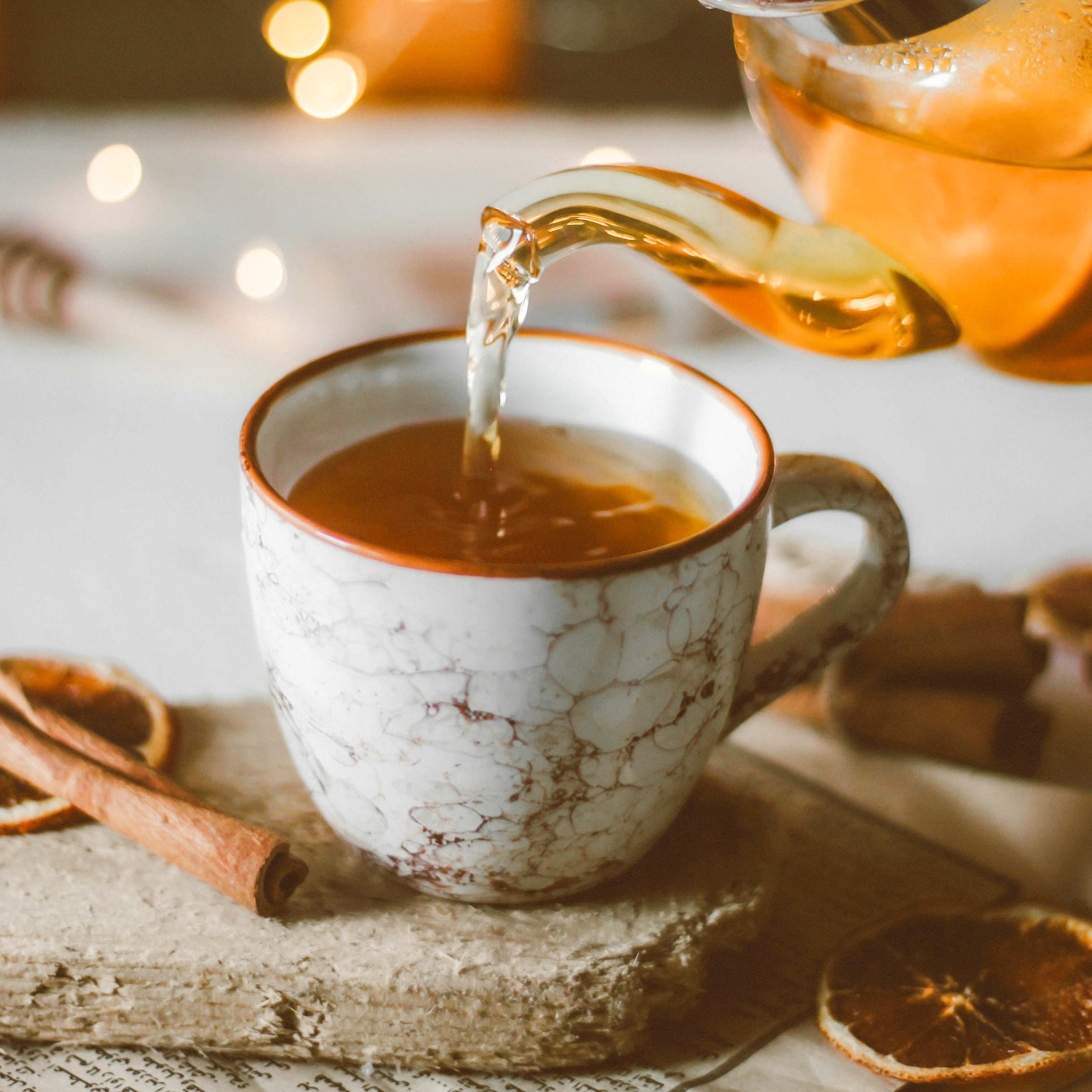 A glass teapot pouring tea into a mug.