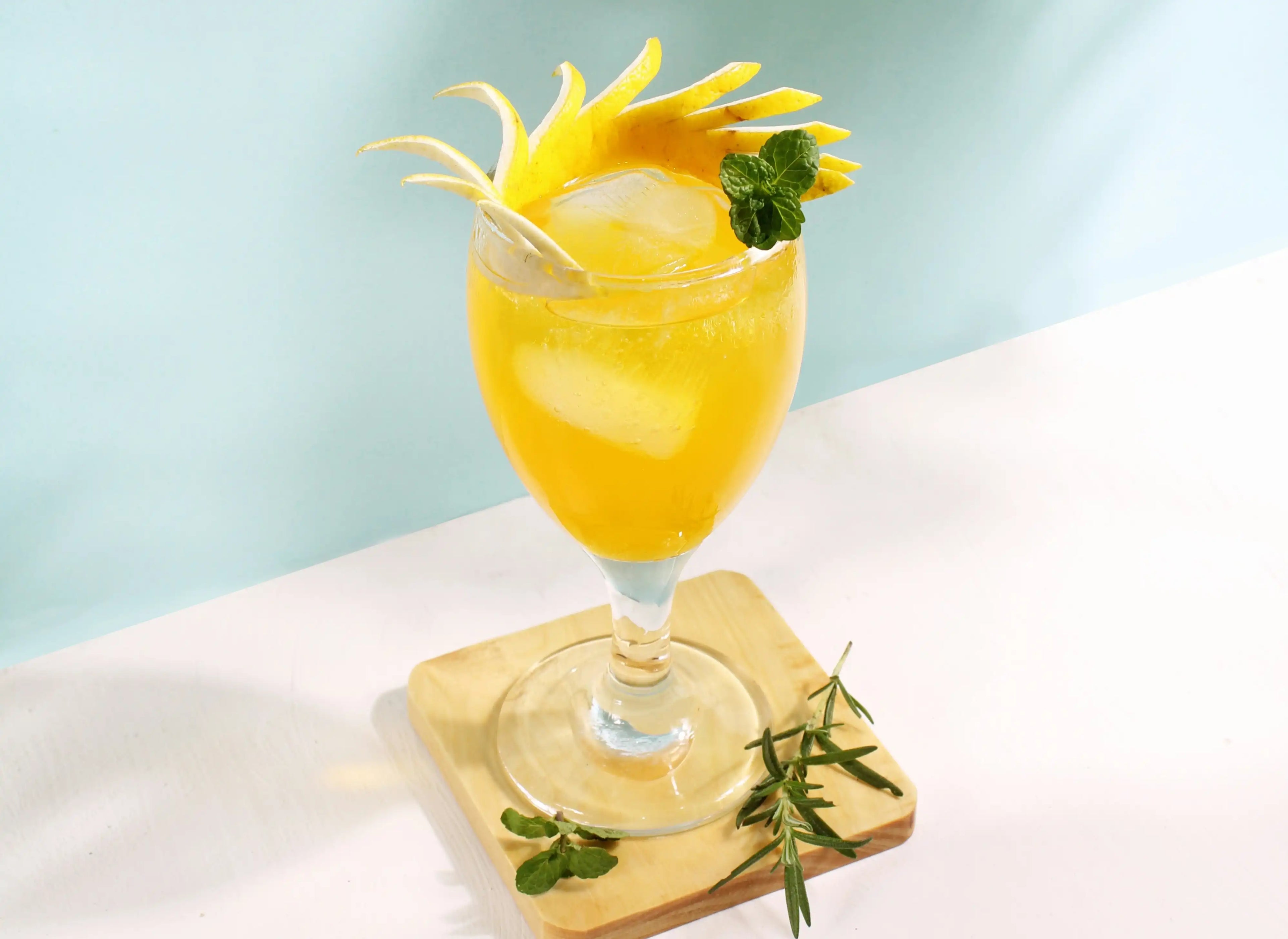glass of an orange colored cocktail garnished with a fringed orange slice and sprig of mint