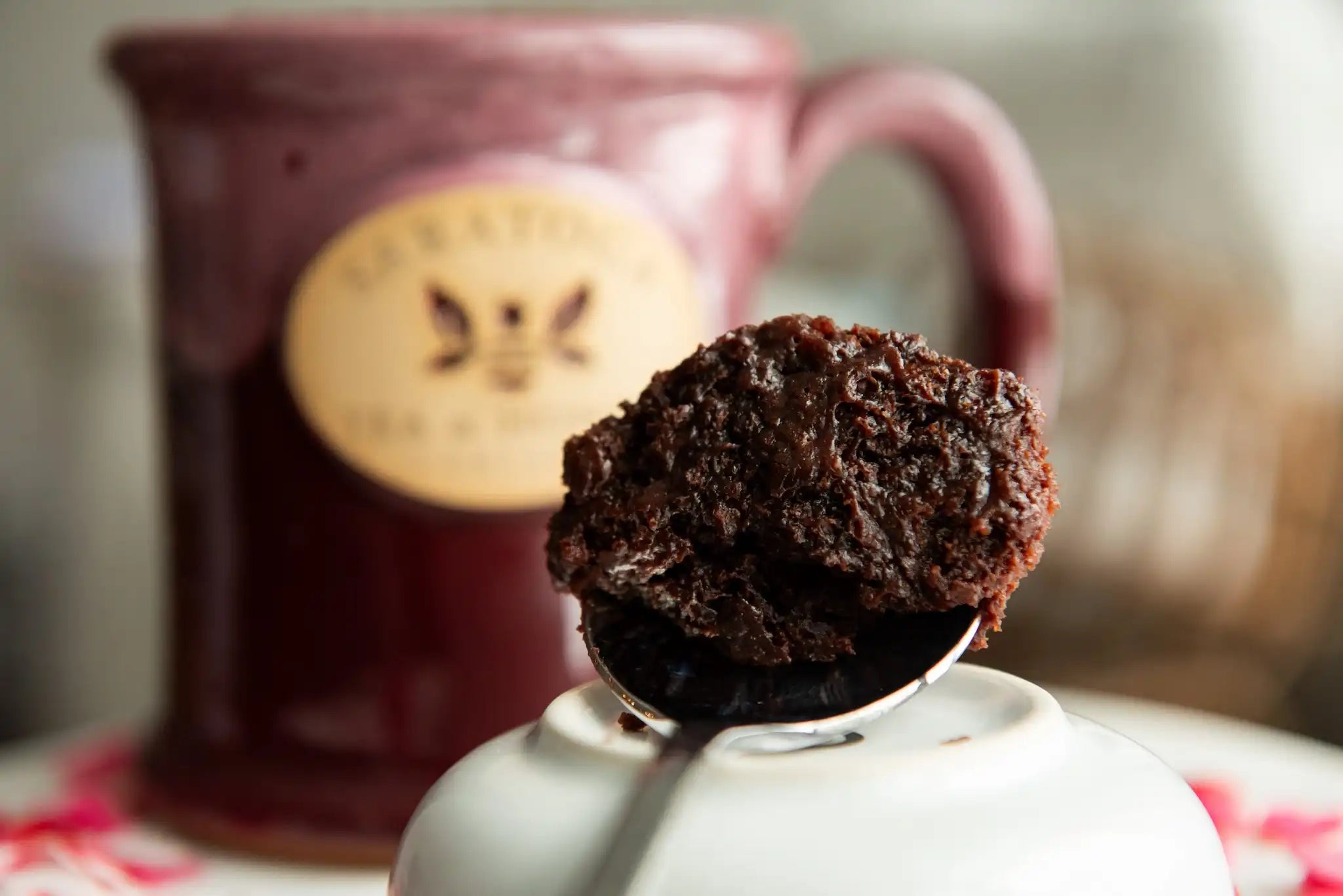 spoon with bite of chocolate black tea mug cake resting in front of pink saratoga tea and honey co mug
