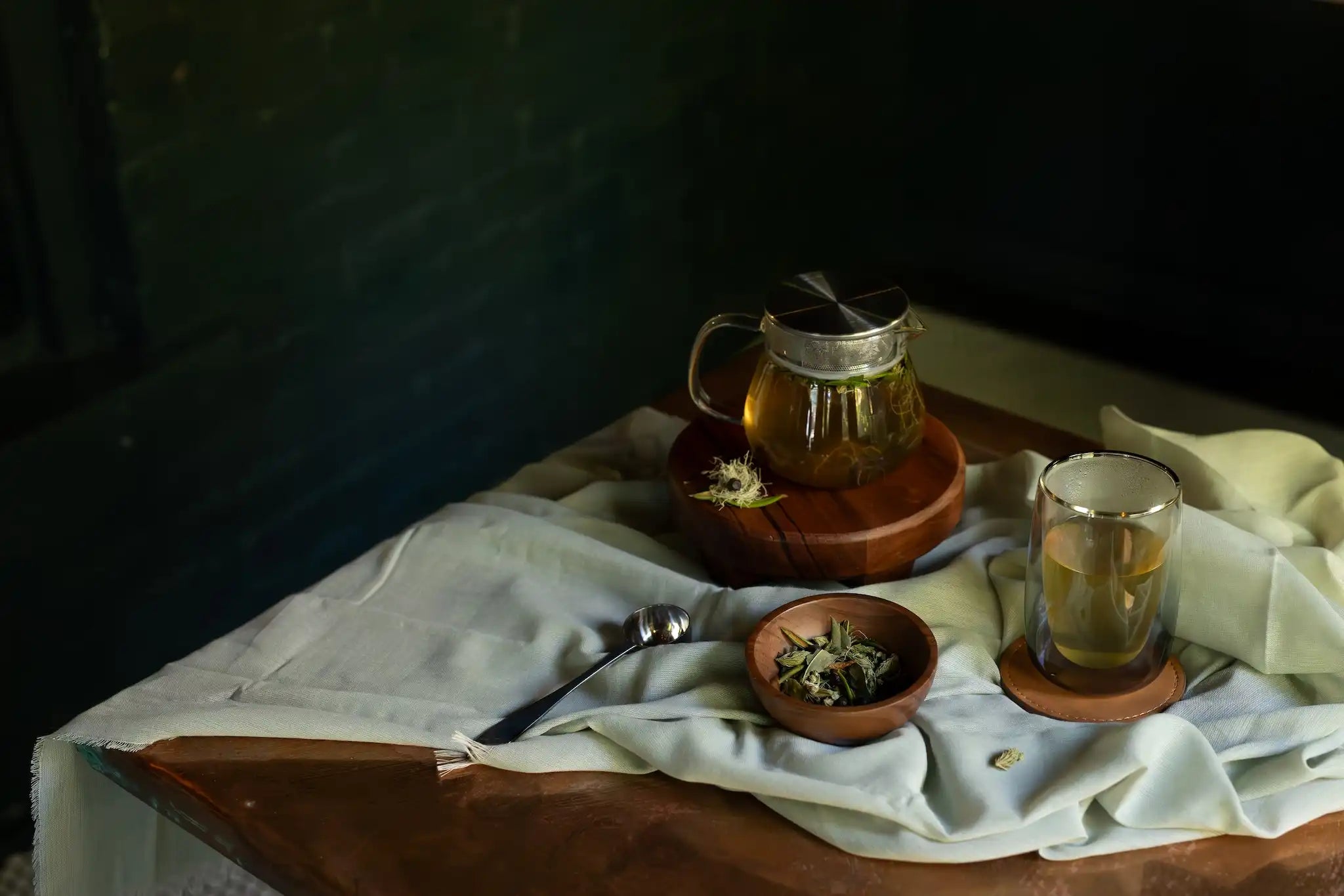 wild taiga herbal tisane in a glass teapot and glass cup against a moody dark background with loose herbs