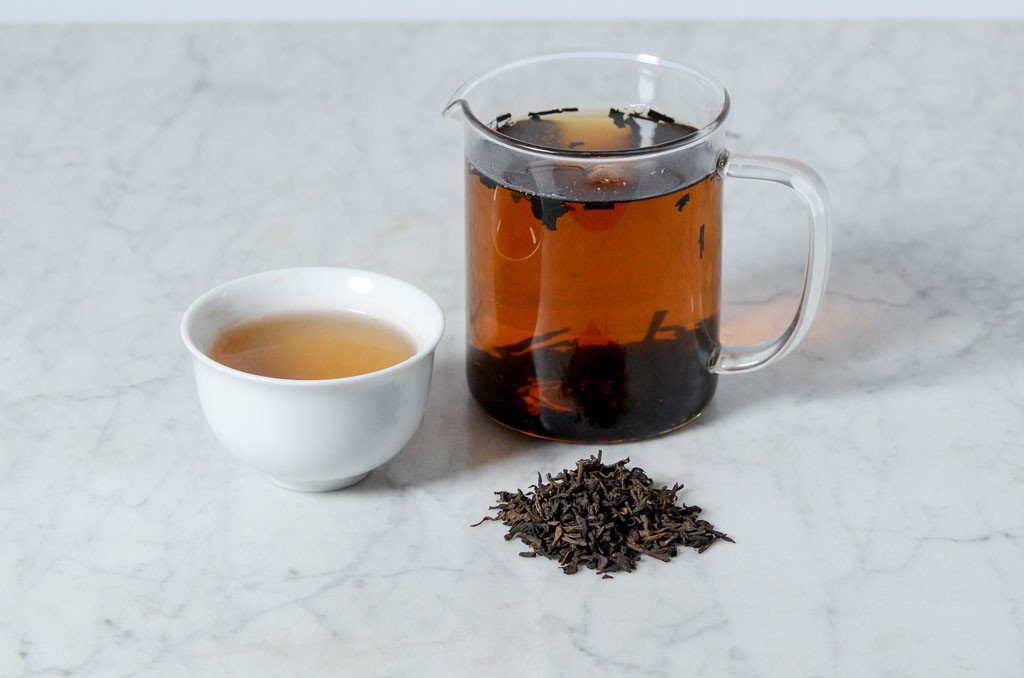 2008 Jingmai aged tea infused in a glass beaker and white cup with a pile of loose pu'er leaves