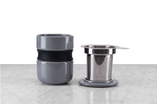 grey Asian-style tea mug with curved silicone grip sitting next to included stainless steel infuser and lid/infuser holder