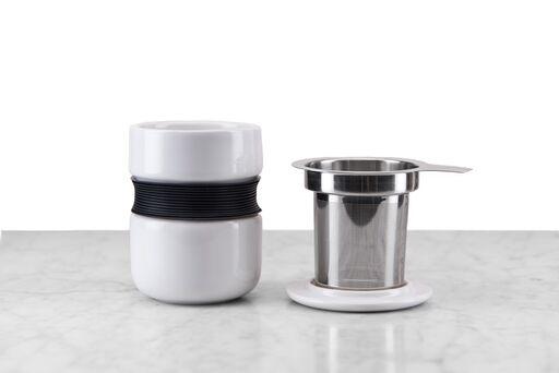 white minimalist tea mug with curved silicone grip sitting next to included infuser and lid/infuser holder