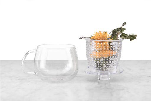 glass mug sitting next to clear infuser and lid filled with a full flower herbal tisane