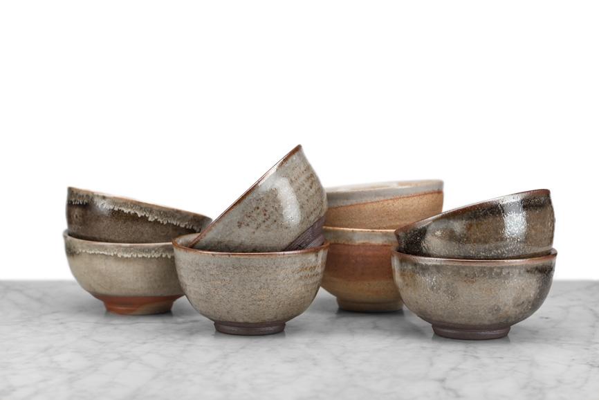 8 tea bowls stacked in four rows of two; glazes all earthy tones with variations in design and color