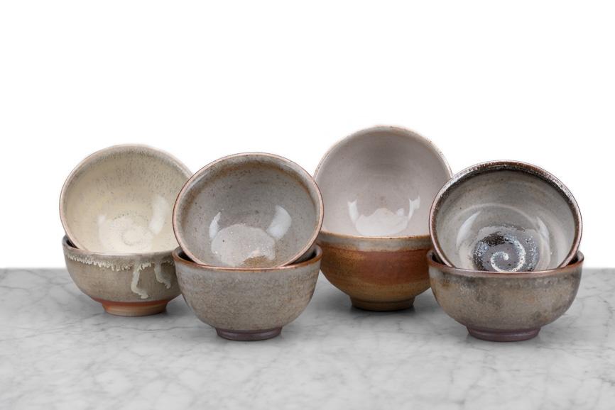 8 hand-thrown tea bowls stacked in four rows of two with top bowls propped to show variations in bowl glaze and design