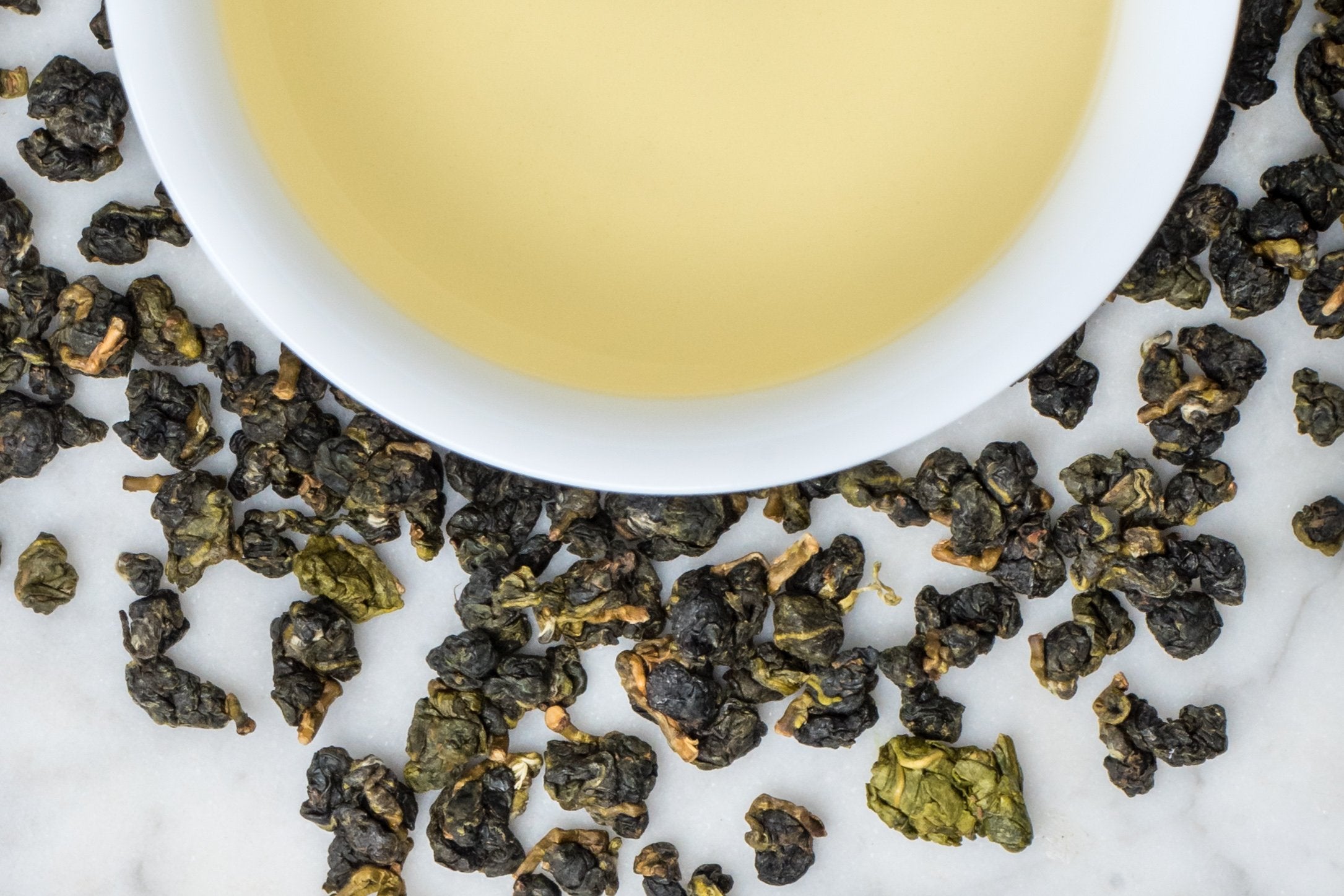 loose leaf rolled high mountain Taiwanese oolong Ali Shan around a white cup with brewed tea