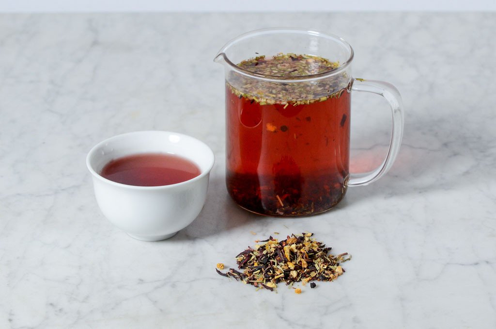 Blood Orange Hibiscus fruity herbal tea shown in a white cup and glass infuser with a pile of loose tea