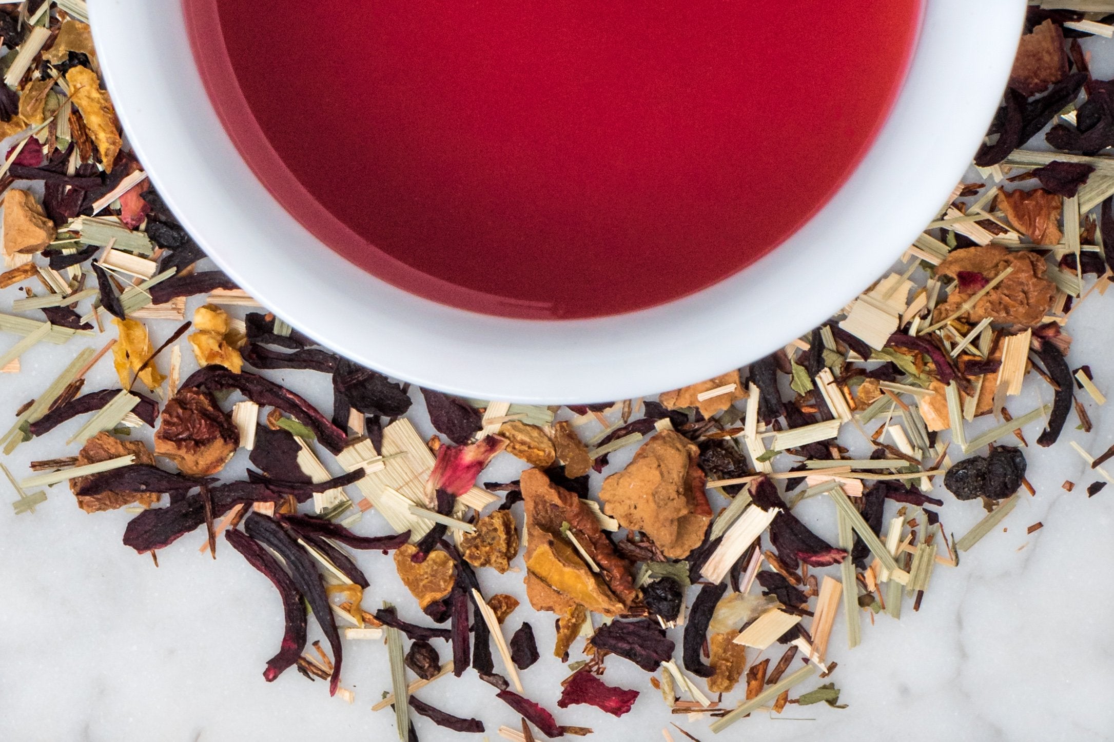 loose leaf blood orange hibiscus tea surrounding a white cup with brewed tea