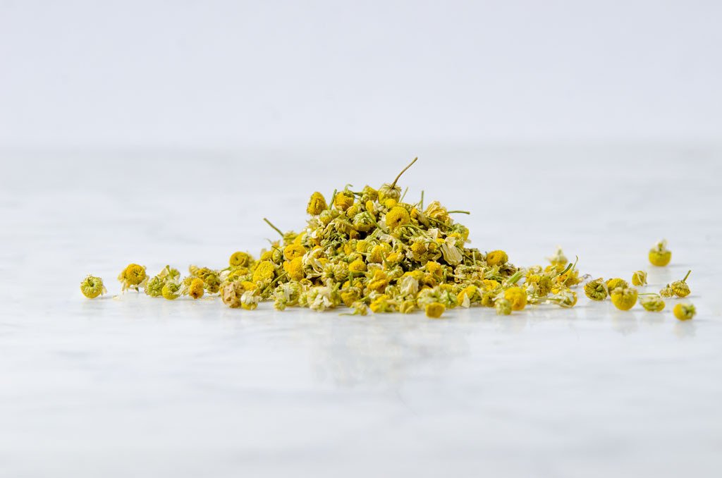 artful pile of whole chamomile flowers for herbal tea on a marble background