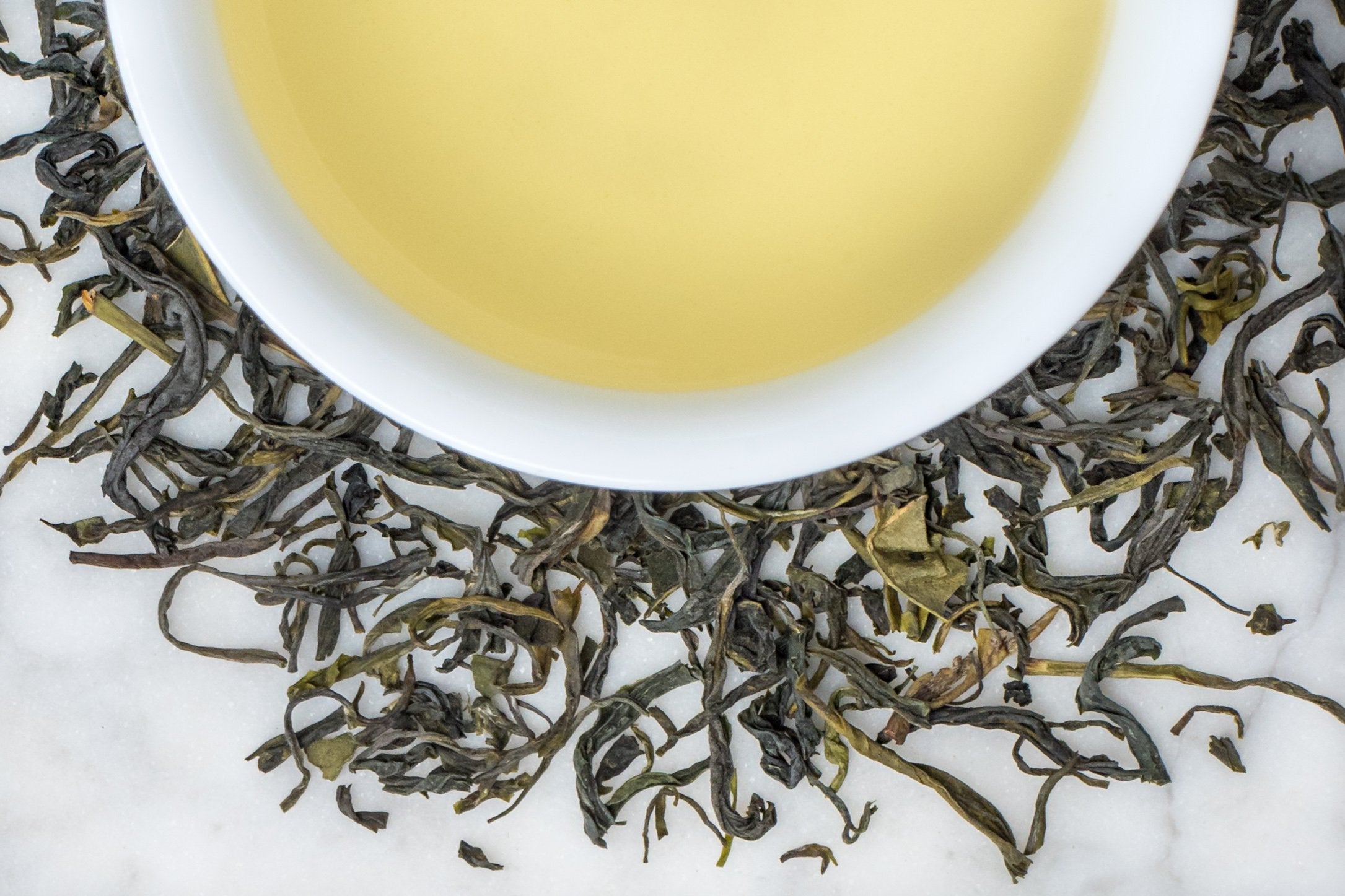 China Green Jade leaves and brewed tea. The twisted green leaves surround a cup of golden-green brewed tea.