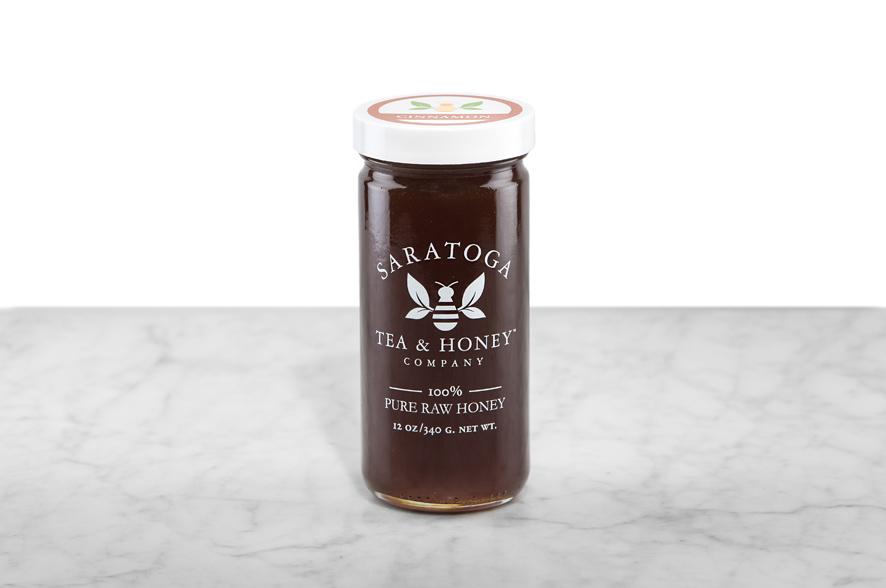 Dark brown Cinnamon Honey displayed in a 12oz cylindrical glass jar with a white lid. The logo and the words: "100% Pure Raw Honey" are printed on the jar.