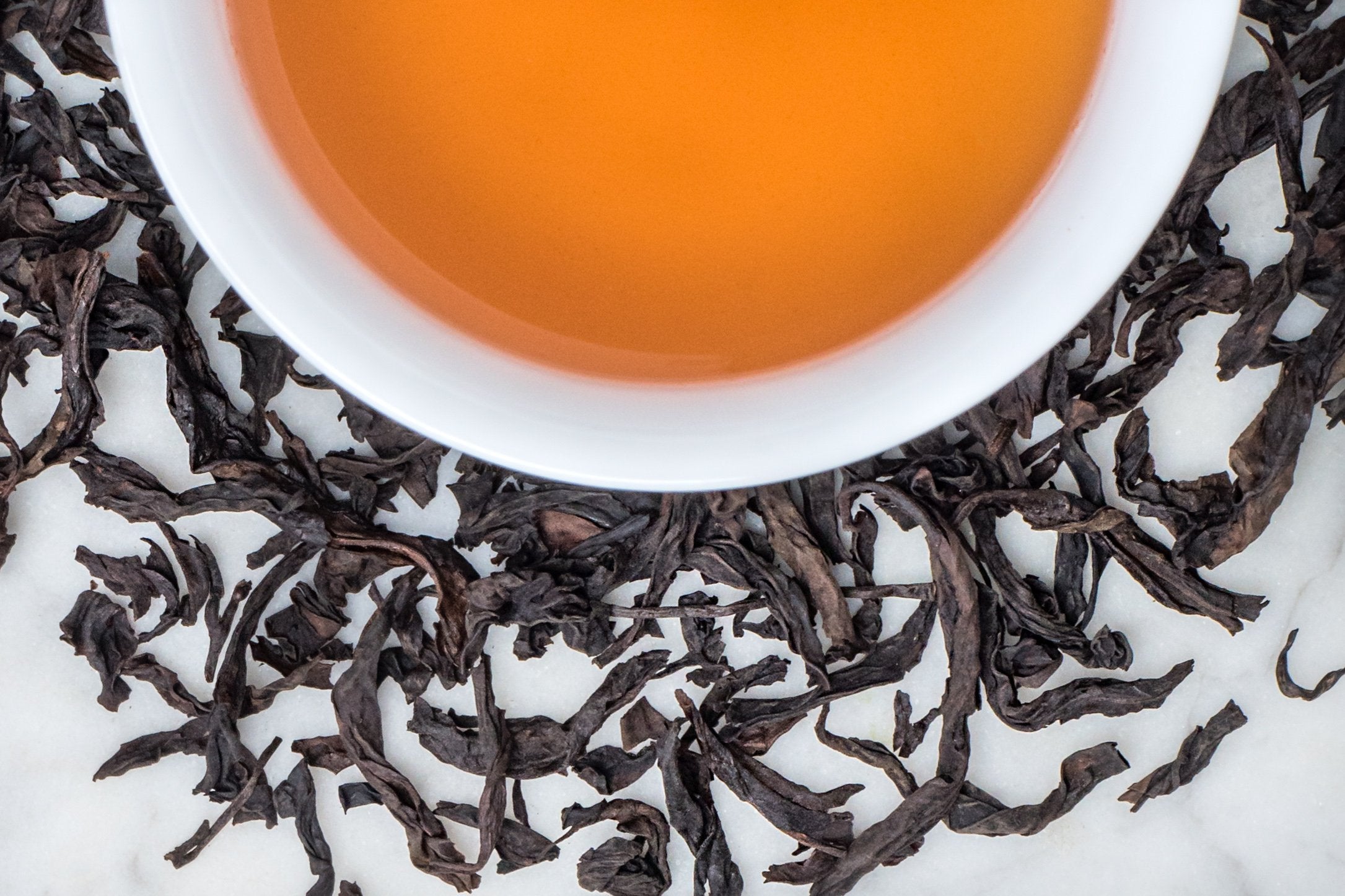loose leaf Da Hong Pao rock oolong surrounding a white cup with brewed oolong