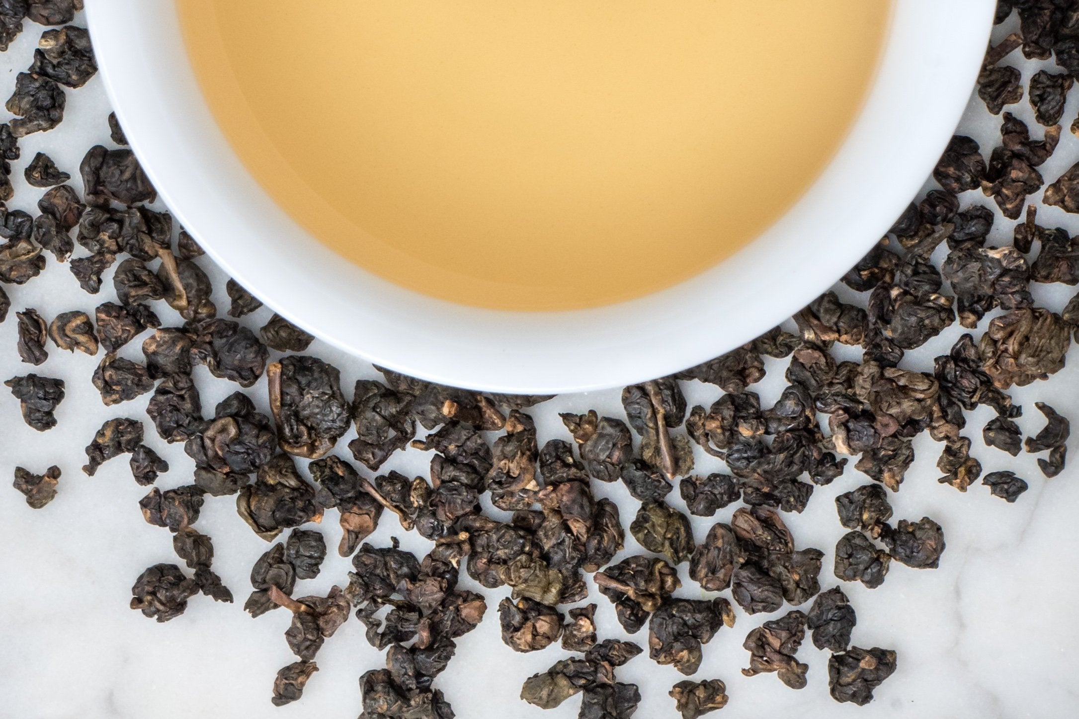 loose leaf rolled Taiwanese oolong Dong Ding surrounding a white cup with brewed tea
