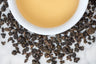 loose leaf rolled Taiwanese oolong Dong Ding surrounding a white cup with brewed tea