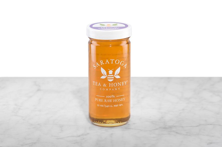 Golden-amber French Lavender Honey displayed in a 12oz cylindrical glass jar with a white lid. The logo and the words: "100% Pure Raw Honey" are printed on the jar.