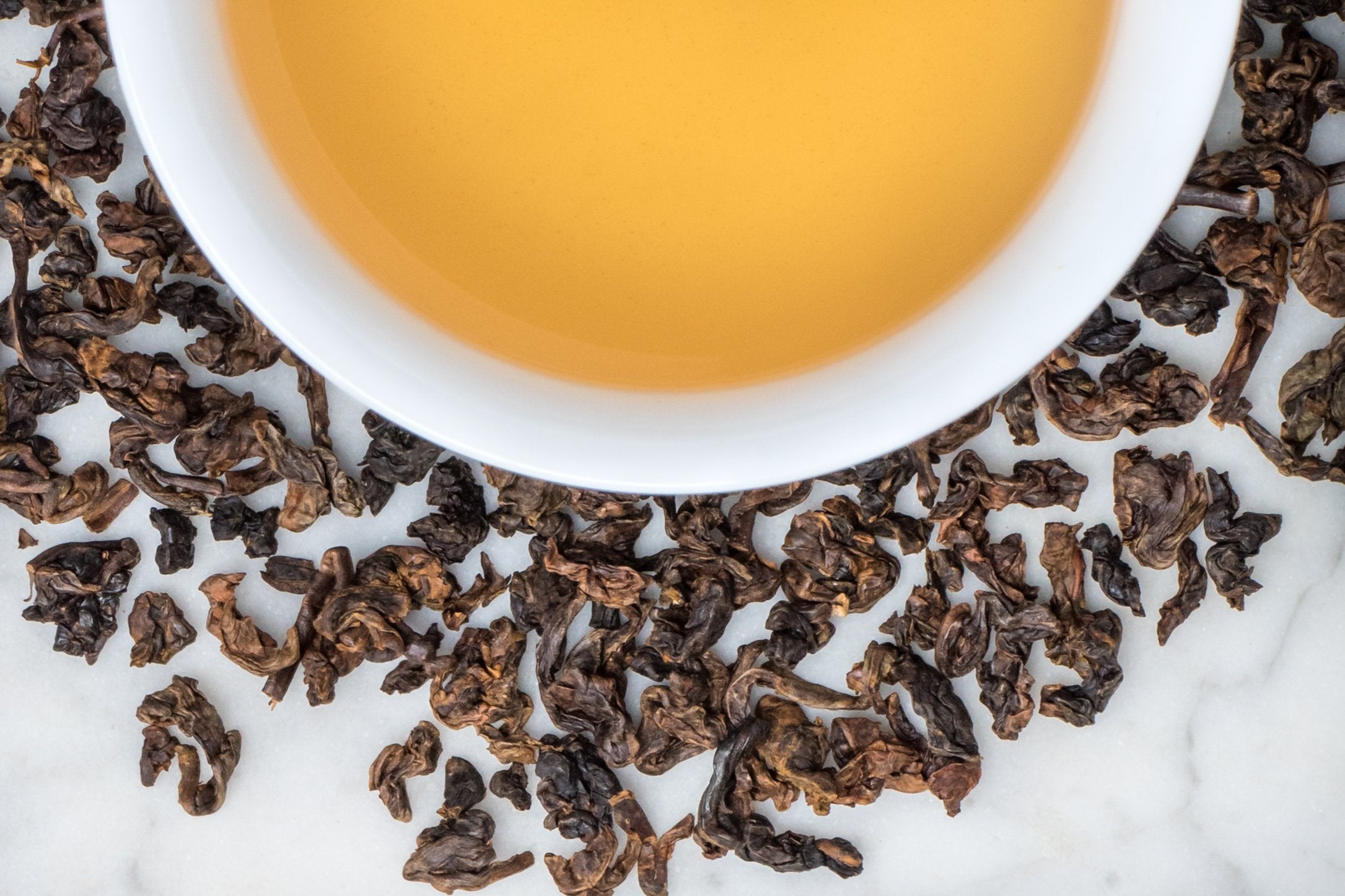 loose leaf rolled gabacha oolong surrounding a white cup with brewed tea