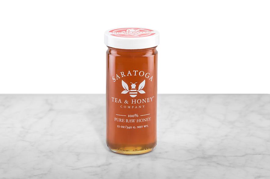 Amber-hued Ghost Pepper Honey displayed in a 12oz cylindrical glass jar with a white lid. The logo and the words: "100% Pure Raw Honey" are printed on the jar.