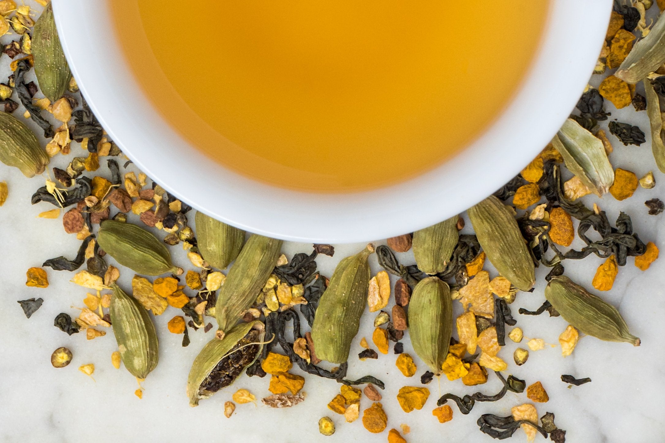 Golden Dragon Chai leaves and brewed tea. Anti-inflammatory turmeric, ginger, green tea, and cardamom surround a cup of yellow-gold colored brewed tea.