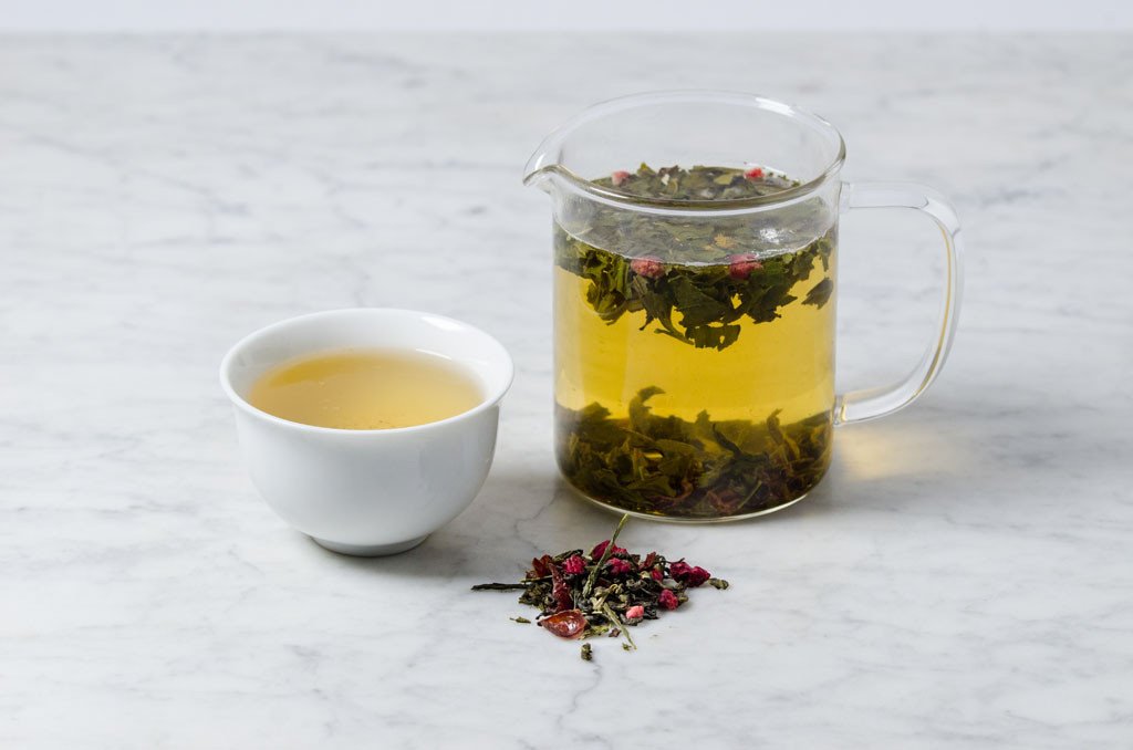 loose leaf pomegranate green tea in a white cup and glass infuser
