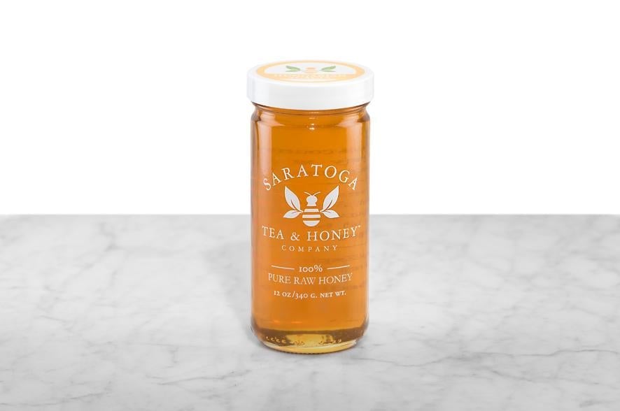 Golden Acacia Honey displayed in a 12oz cylindrical glass jar with a white lid. The logo and the words: "100% Pure Raw Honey" are printed on the jar.