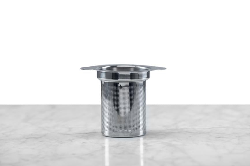 side view of a stainless steel tea infuser sitting on a marble and white background