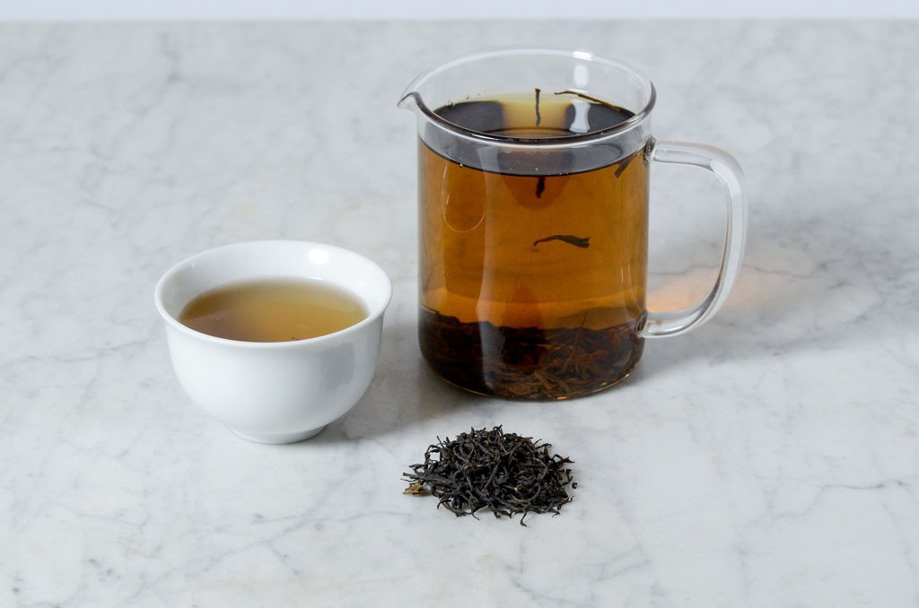 Keemun Mao Feng infusion in a cup and glass infuser next to a pile of loose leaf black tea leaves