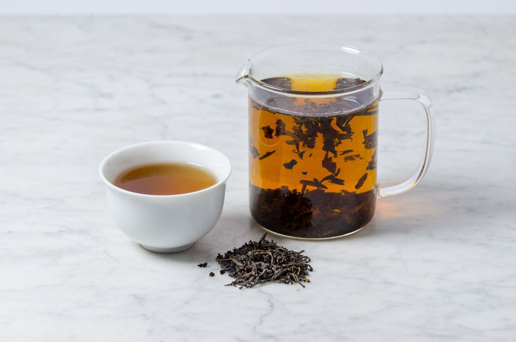 lapsang souchong brewed in a white cup and glass infuser beside a pile of loose leaf tea