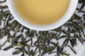 Lu An Gua Pian green tea with distinctive blue-tinged loose leaves surrounding white cup filled with brewed green tea