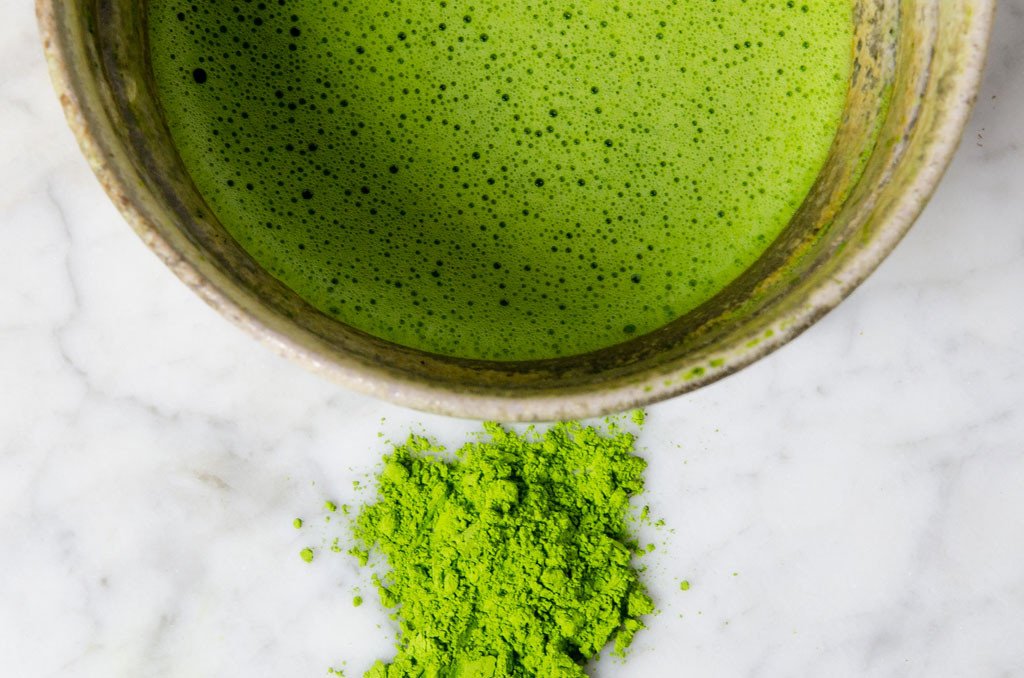 vibrantly green matcha powder next to a bowl of matcha with beautiful matcha crema