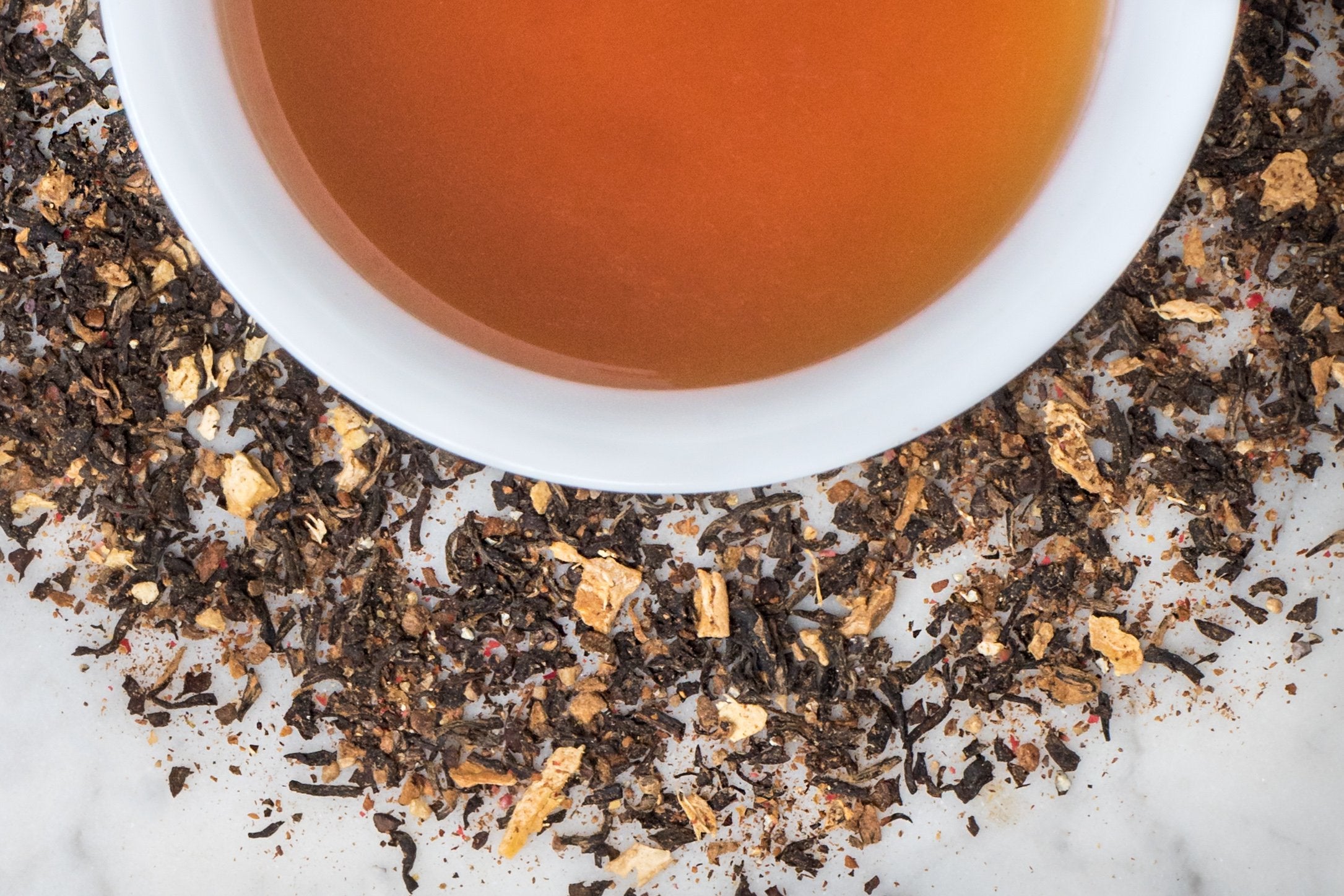 Masala Chai leaves and brewed tea. Fine black tea, cinnamon, ginger and other spices surround a cup of amber-brown brewed tea.