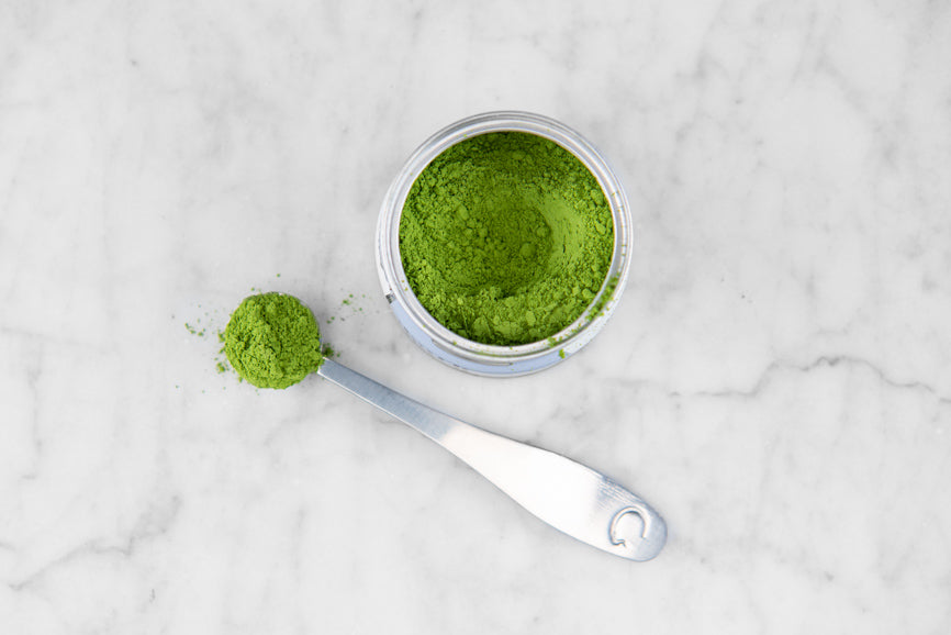 spoon of matcha next to tin of bright green matcha powder