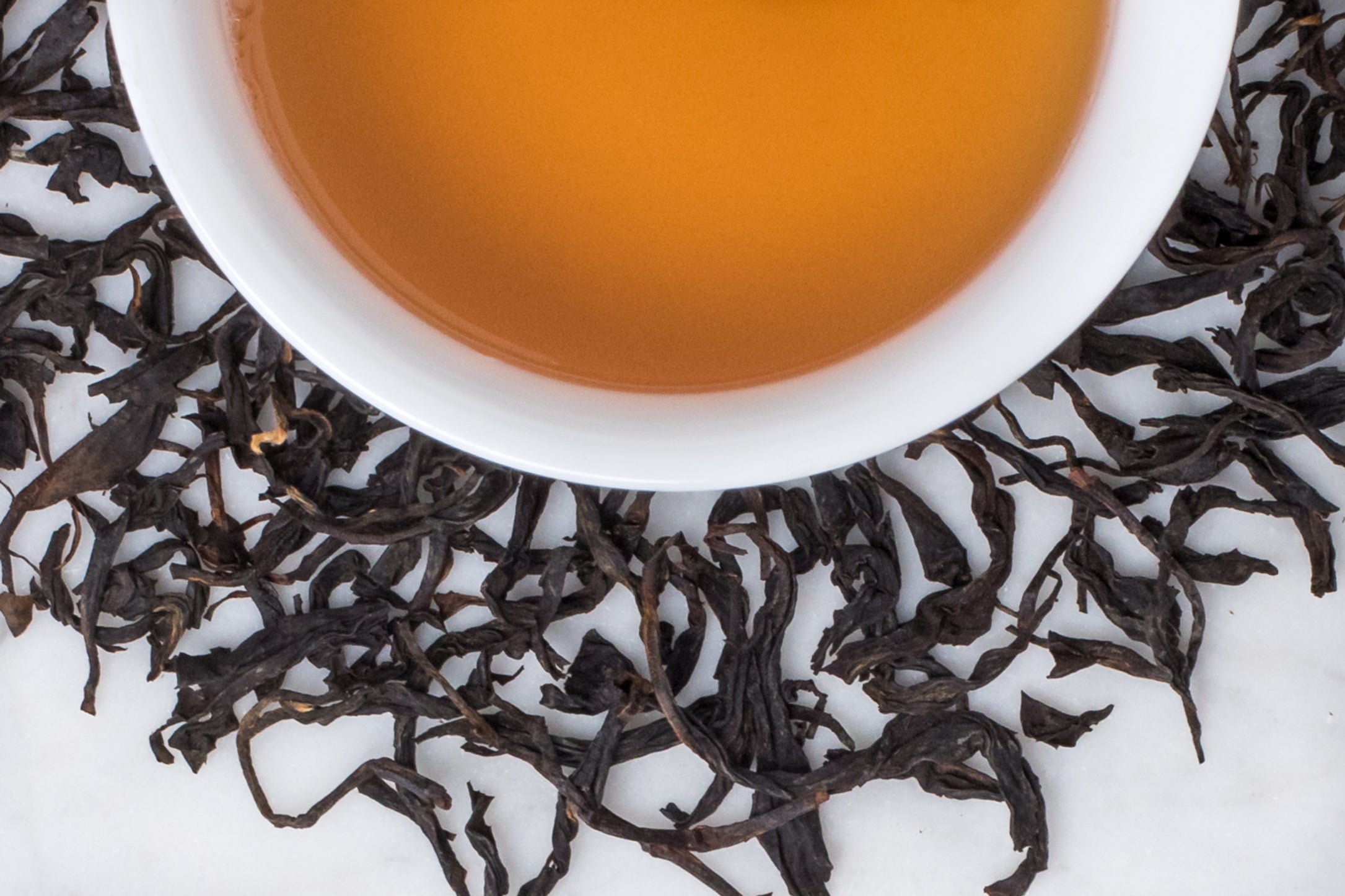 Mi Xiang Hong Cha black tea leaves and brewed tea. Large, twisted black tea leaves surround a cup of light amber-hued brewed black tea.