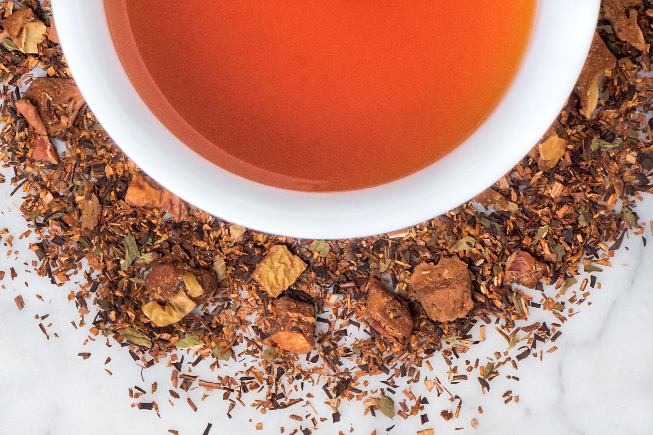 loose leaf mint and chocolate rooibos herbal tea surrounding a white cup with brewed tea