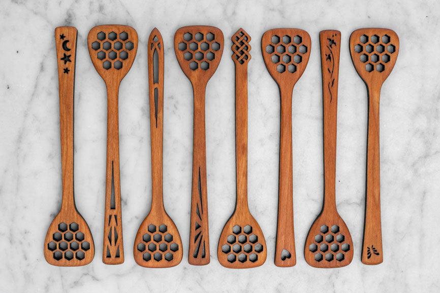 wooden honey dippers with different designs alternating in a row on a marble background