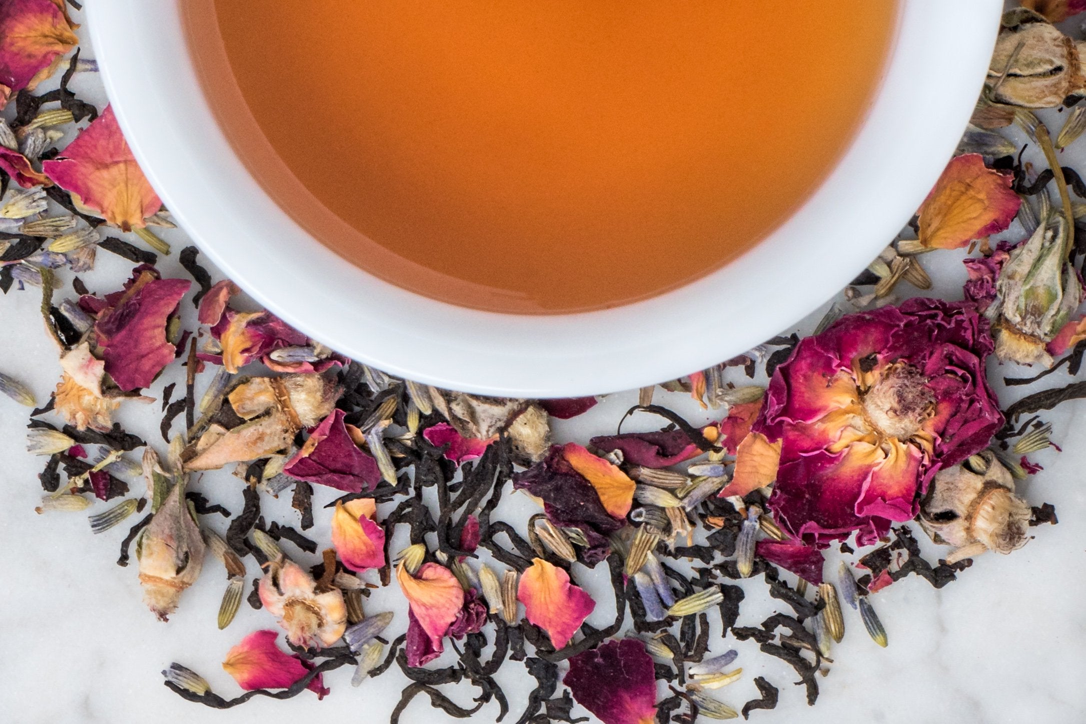 Paris in Love leaves and brewed tea. Black tea leaves, lavender buds, and rose petals surround a cup of amber-hued brewed tea.