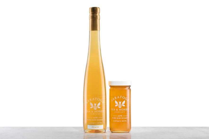 Golden-amber Peach Infused Honey displayed in two glass jars with the logo and the words: "100% Pure Raw Honey". Left: Tall, 19oz bottle shaped like a wine bottle and capped with a cork. Right: 12oz cylindrical bottle with white cap. 