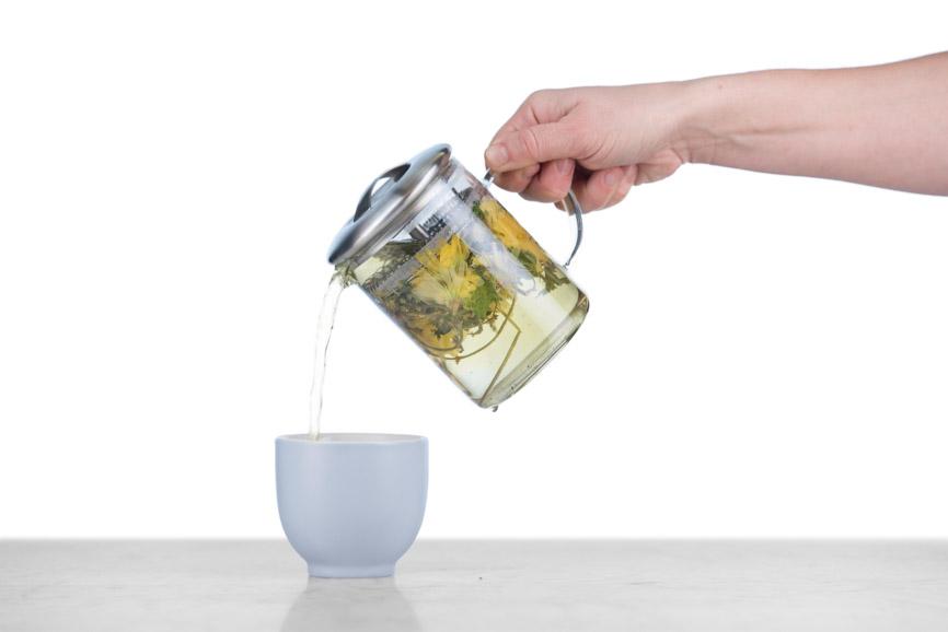 pouring herbal tisane into a grey cup from a glass tea infuser